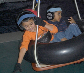 two children sitting in a tire swing together; each with headphones on