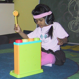 child sitting on the floor with a plastic mallet in her hand, playing with a toy