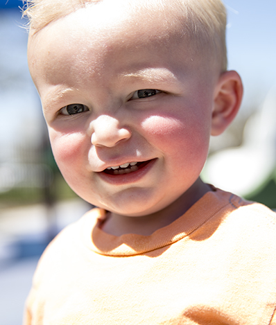 young toddler looks at the camera smiling as the sun reflects off his face